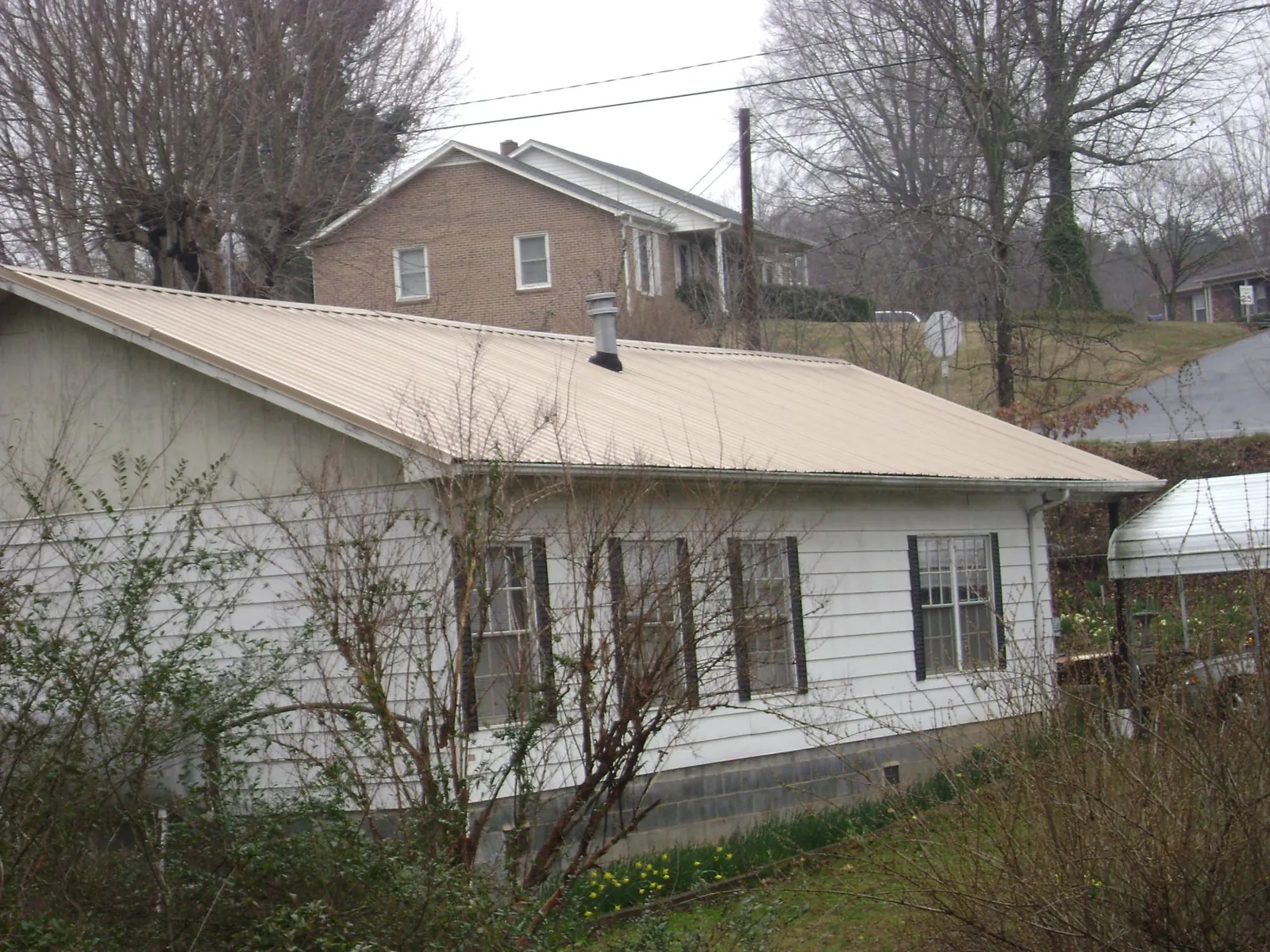 Tan metal roof on a white sided house set into a hillside — Commercial Roofing by Roofing Brothers in Boiling Springs